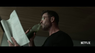 a man drinking from a bottle while holding a piece of paper