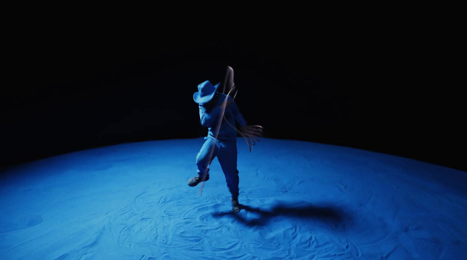 a man in a white suit and hat standing in the dark