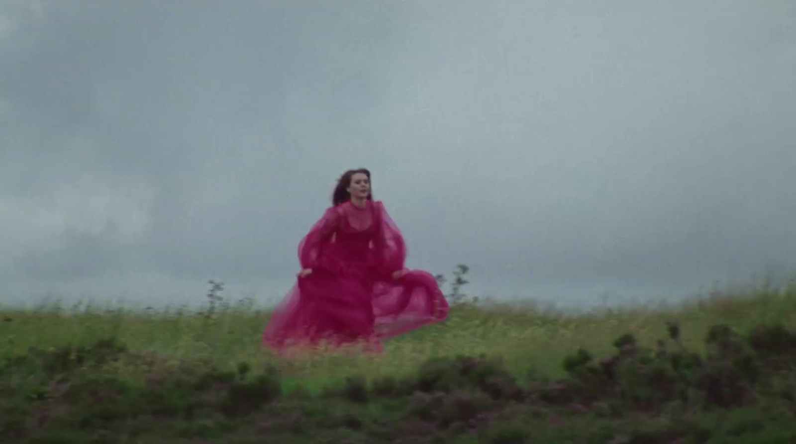 a woman in a pink dress is walking in a field