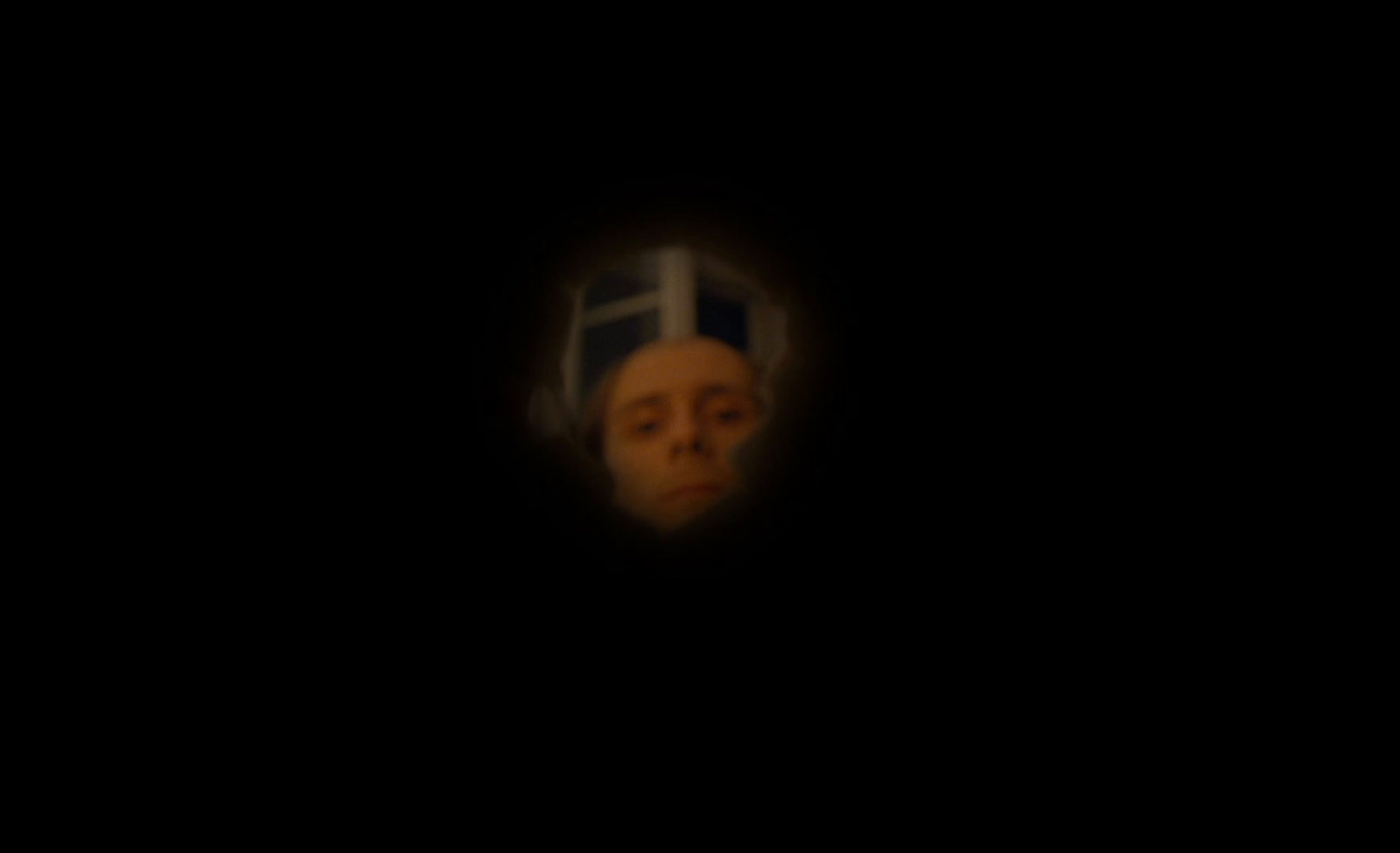 a man's face is seen through a hole in the dark