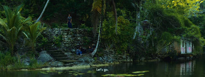 a group of people standing on the side of a river next to a lush green