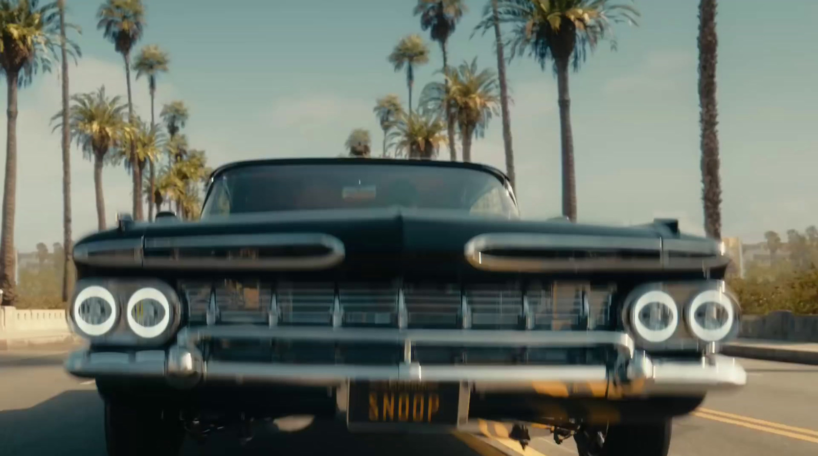 a black car driving down a street next to palm trees