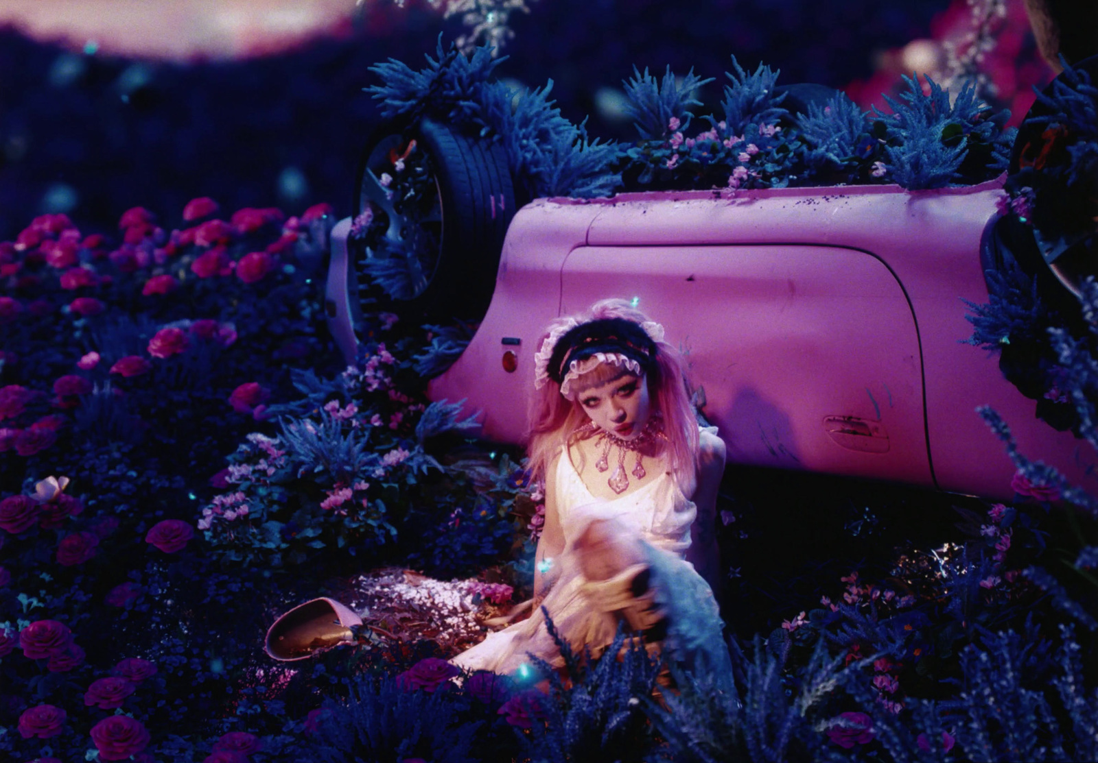 a woman sitting in a field of flowers next to a pink car