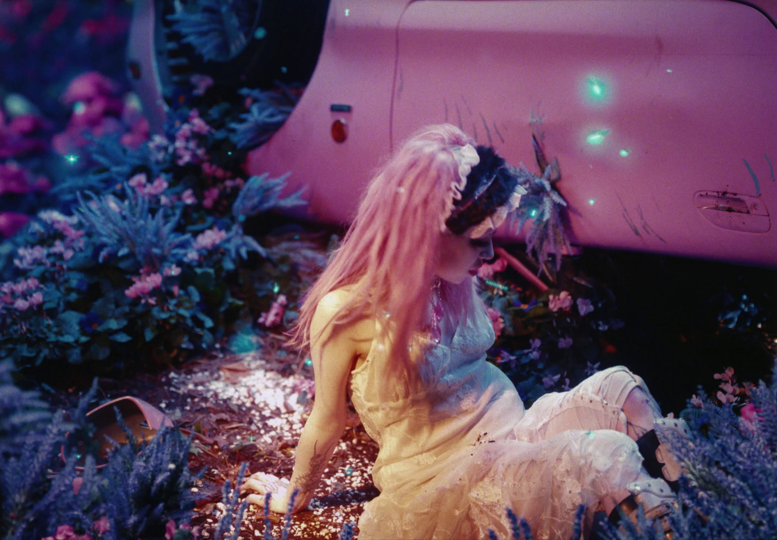 a woman sitting on the ground next to a pink car