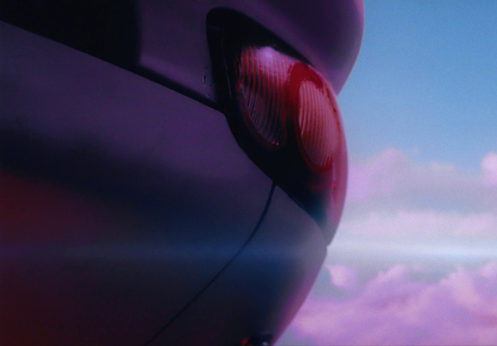 a close up of a car tail light with clouds in the background