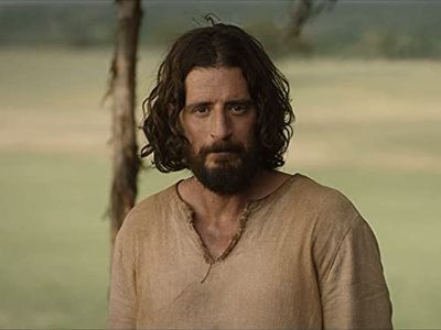 a man with long hair and a beard standing in front of a tree