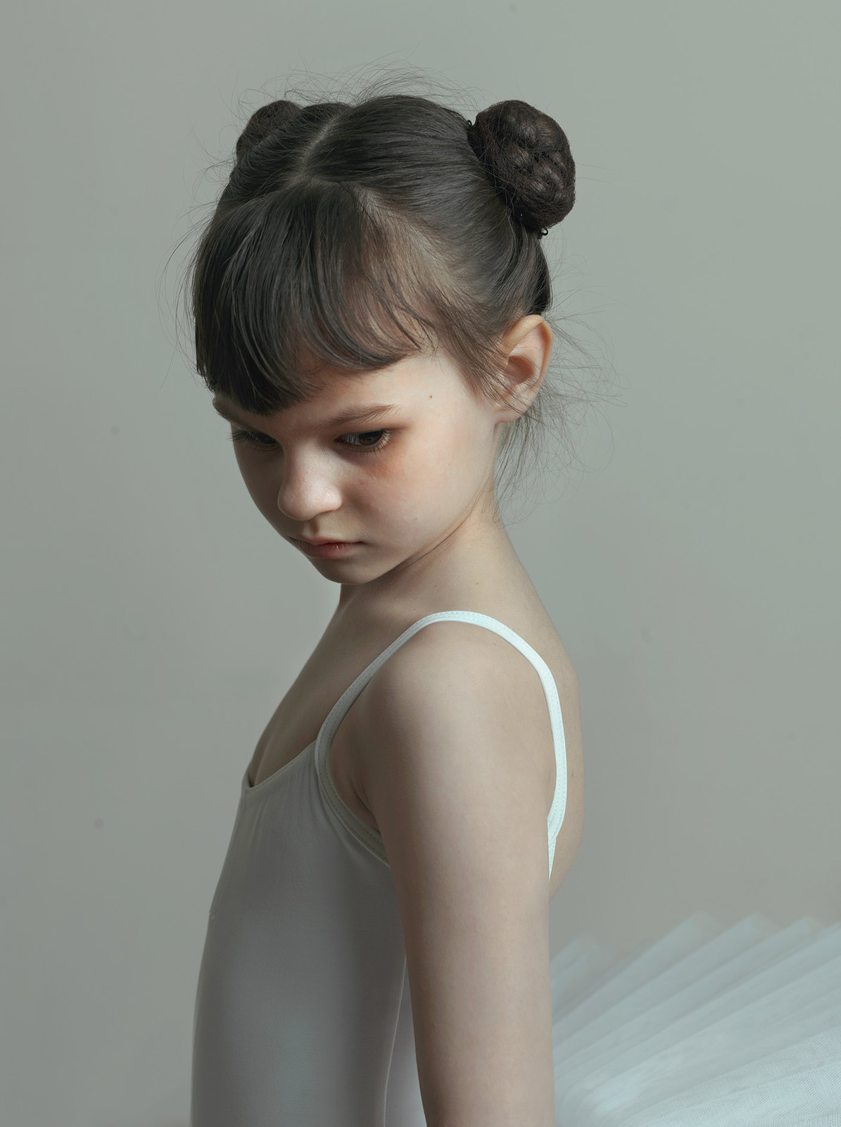 a little girl in a white leotard with a bun in her hair