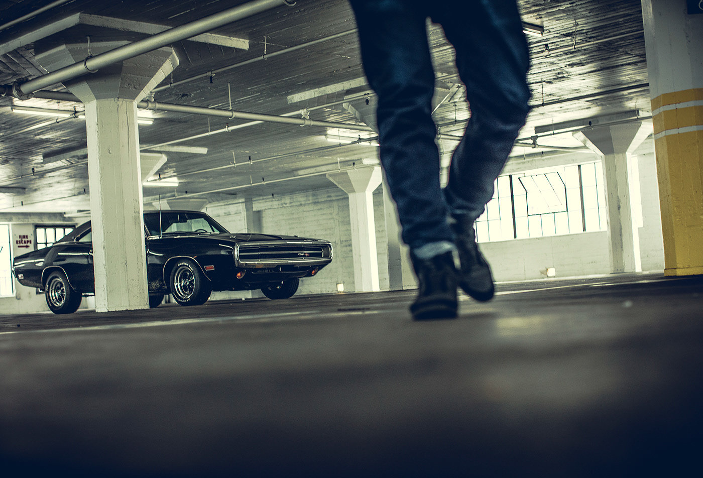 a man walking in a parking garage next to a black car