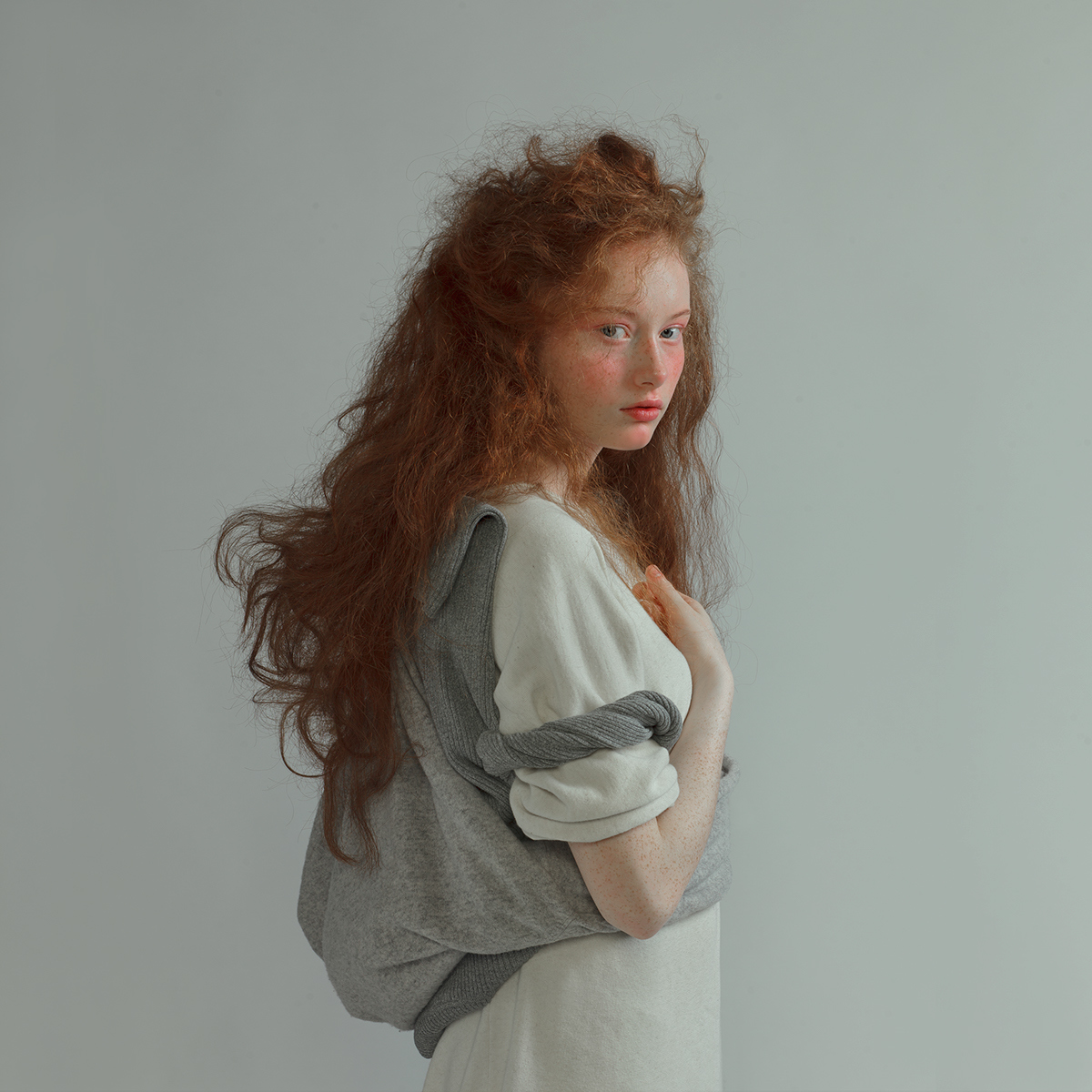 a woman with long red hair standing in front of a white wall