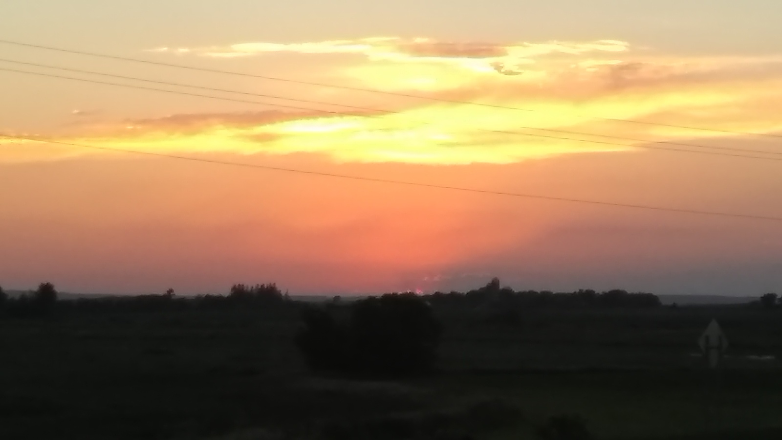 the sun is setting over a field with power lines