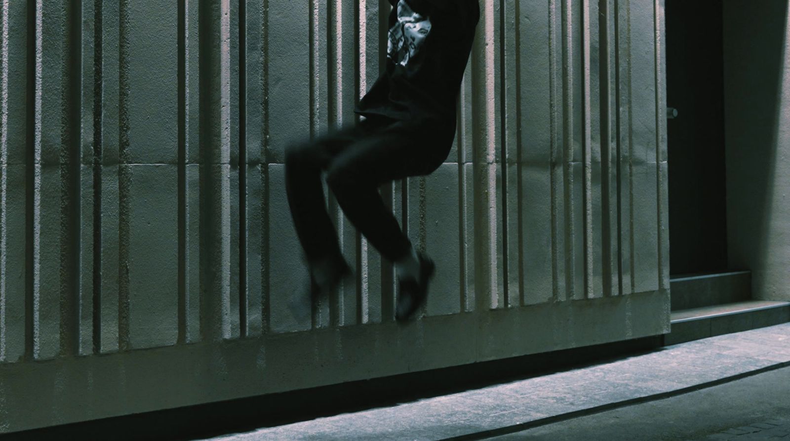 a man in a black suit leaning against a wall