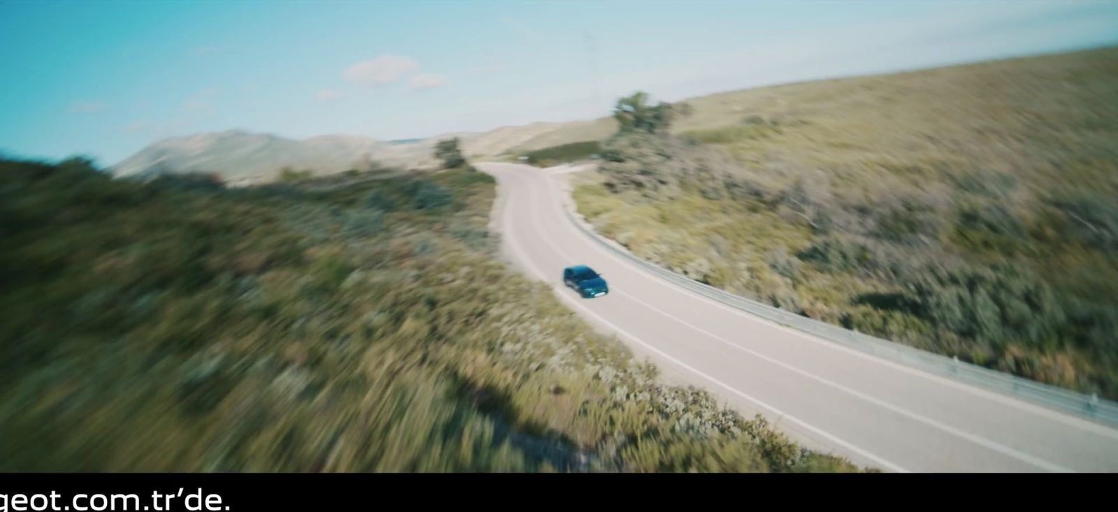 a blue car driving down a road next to a lush green hillside