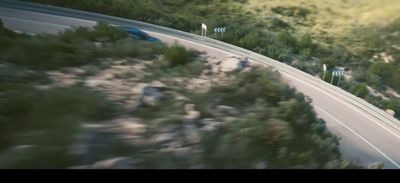 a car driving down a road next to a lush green hillside