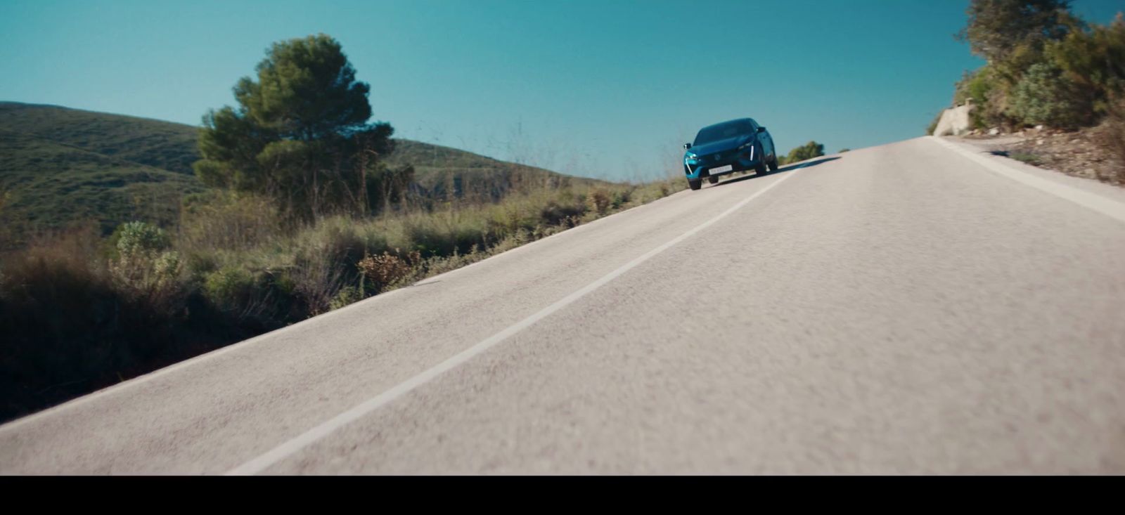 a blue car driving down a road next to a hill