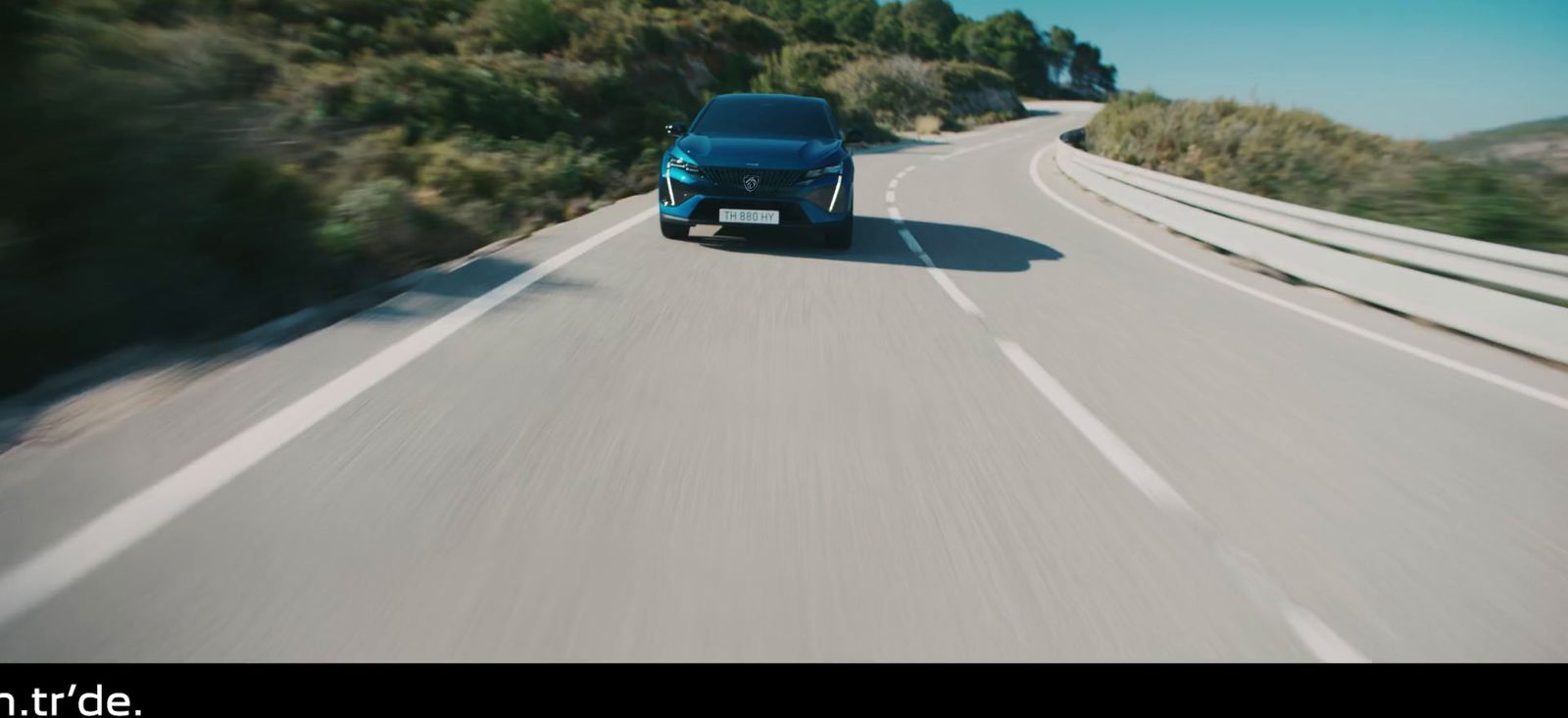 a blue car driving down a road next to a forest