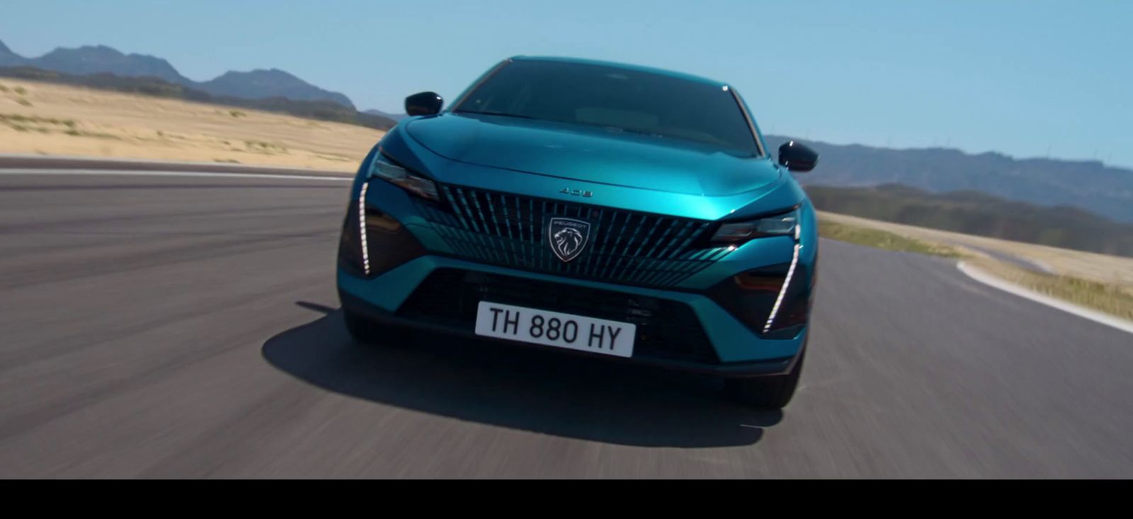 a blue car driving down a road with mountains in the background