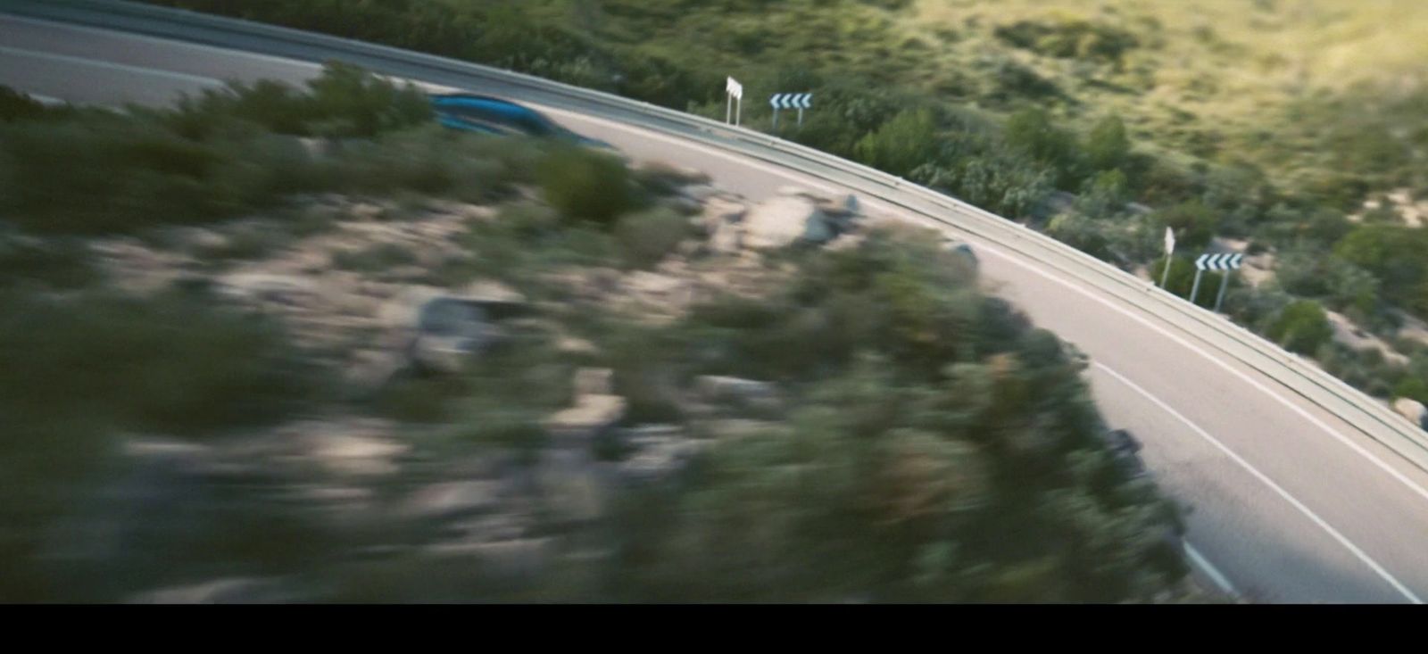 a car driving down a road next to a lush green hillside