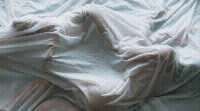 a person laying in a bed covered in white sheets