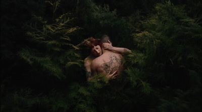 a man with a tattoo on his chest laying in a forest