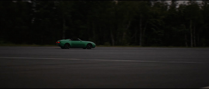 a green car driving down a road next to a forest