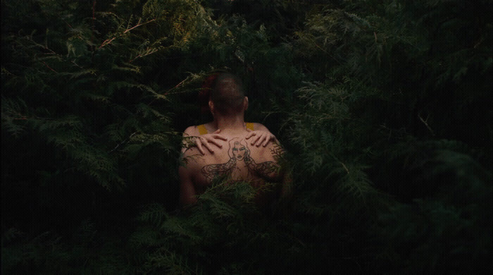 a man with tattoos standing in a forest