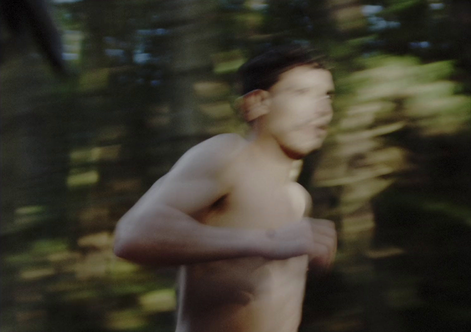 a shirtless man running through a forest