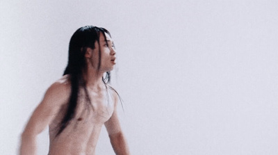 a man with long hair and no shirt standing in front of a white wall