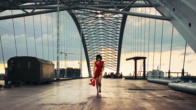 a woman in a red dress walking across a bridge