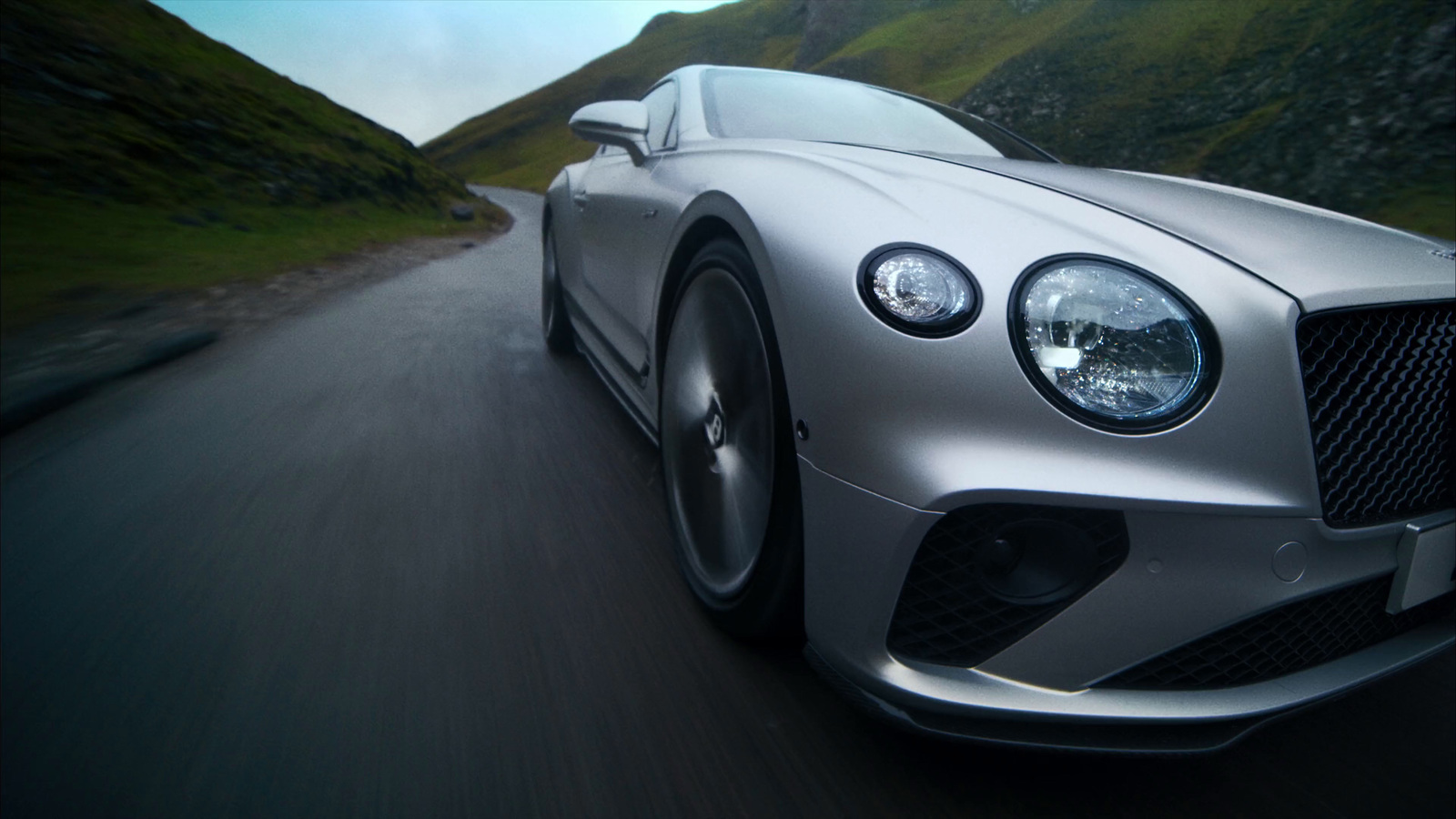 a silver sports car driving down a mountain road