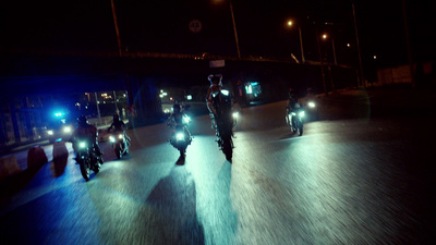 a group of people riding motorcycles down a street at night