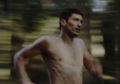 a man without a shirt running in the woods