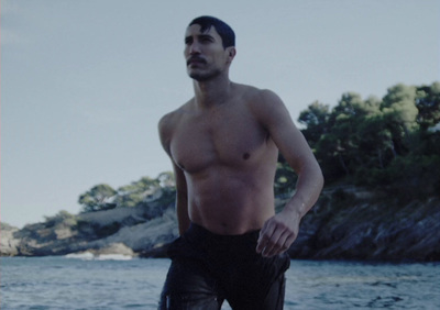 a shirtless man standing on a beach next to a body of water