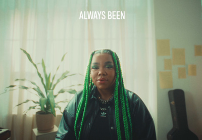 a woman with green dreadlocks sitting in front of a plant