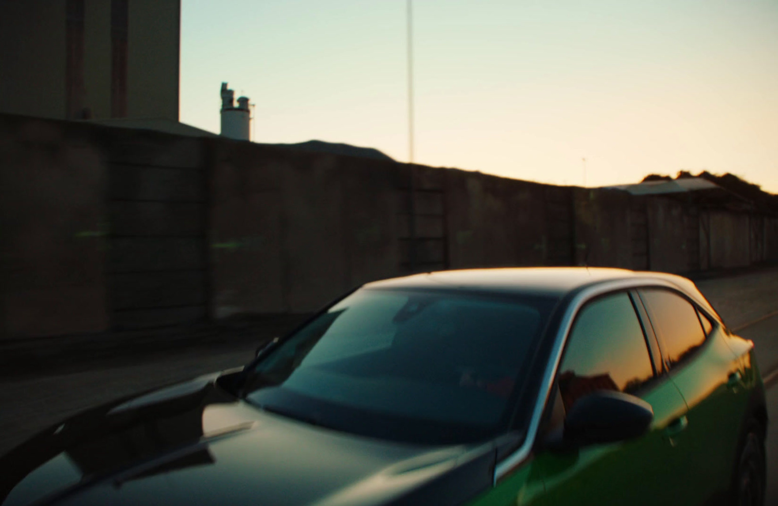 a green car driving down a street next to a tall building