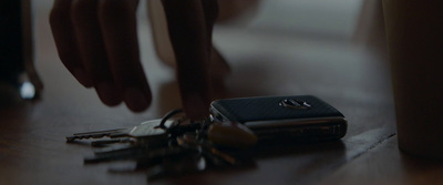 a hand reaching for a cell phone next to a bunch of keys