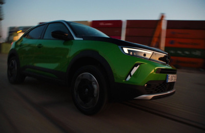 a green car driving down a street next to a fence