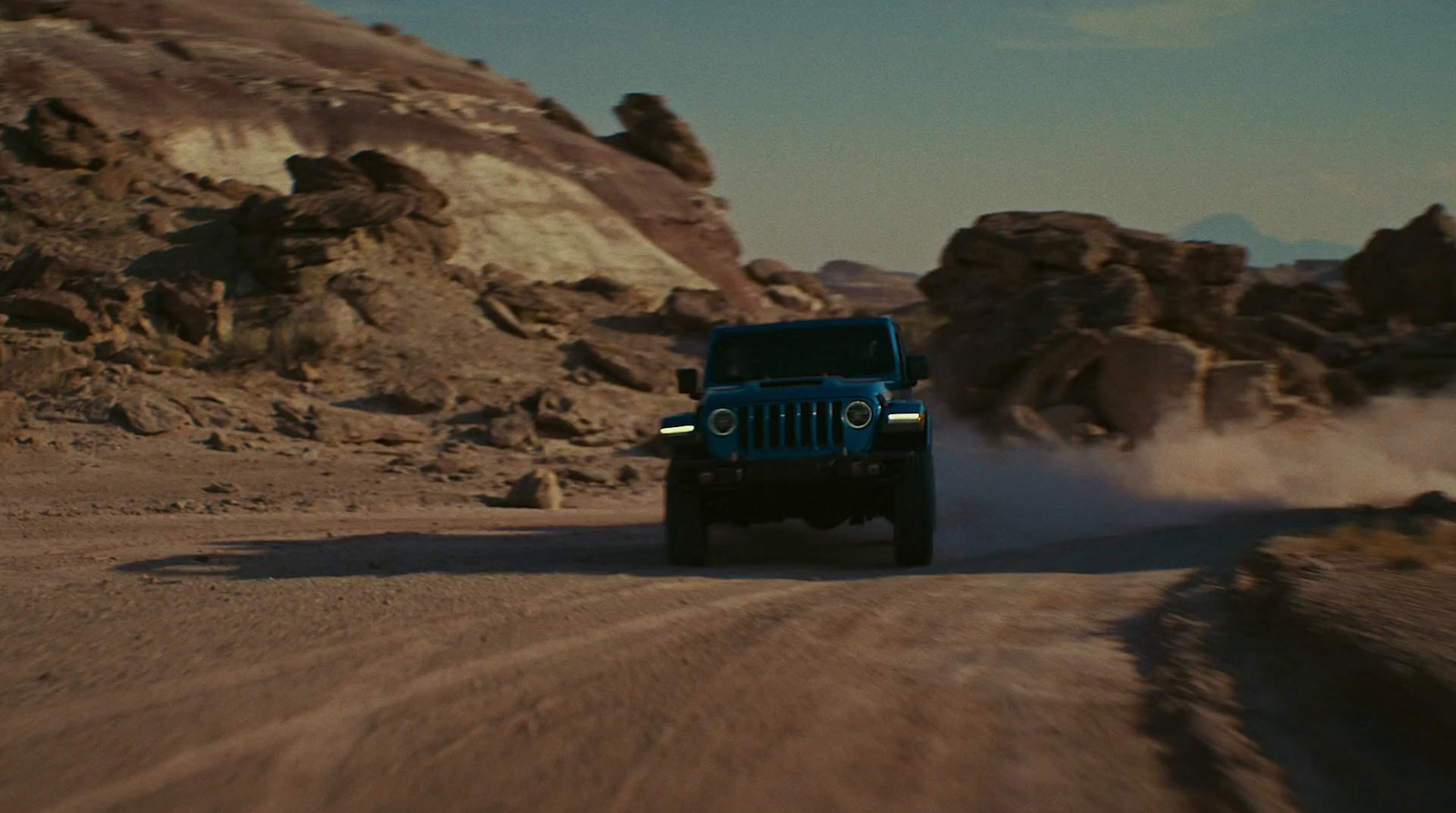 a blue jeep driving down a dirt road