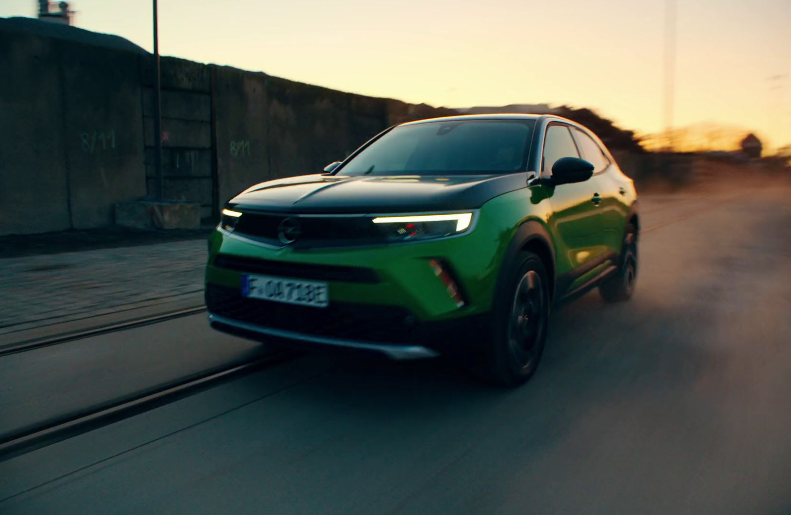 a green car driving down a street at sunset