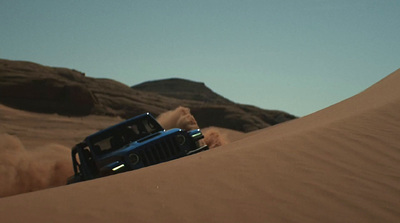 a jeep driving through the desert with a mountain in the background