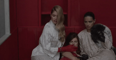 three women in white robes sitting on a red bench