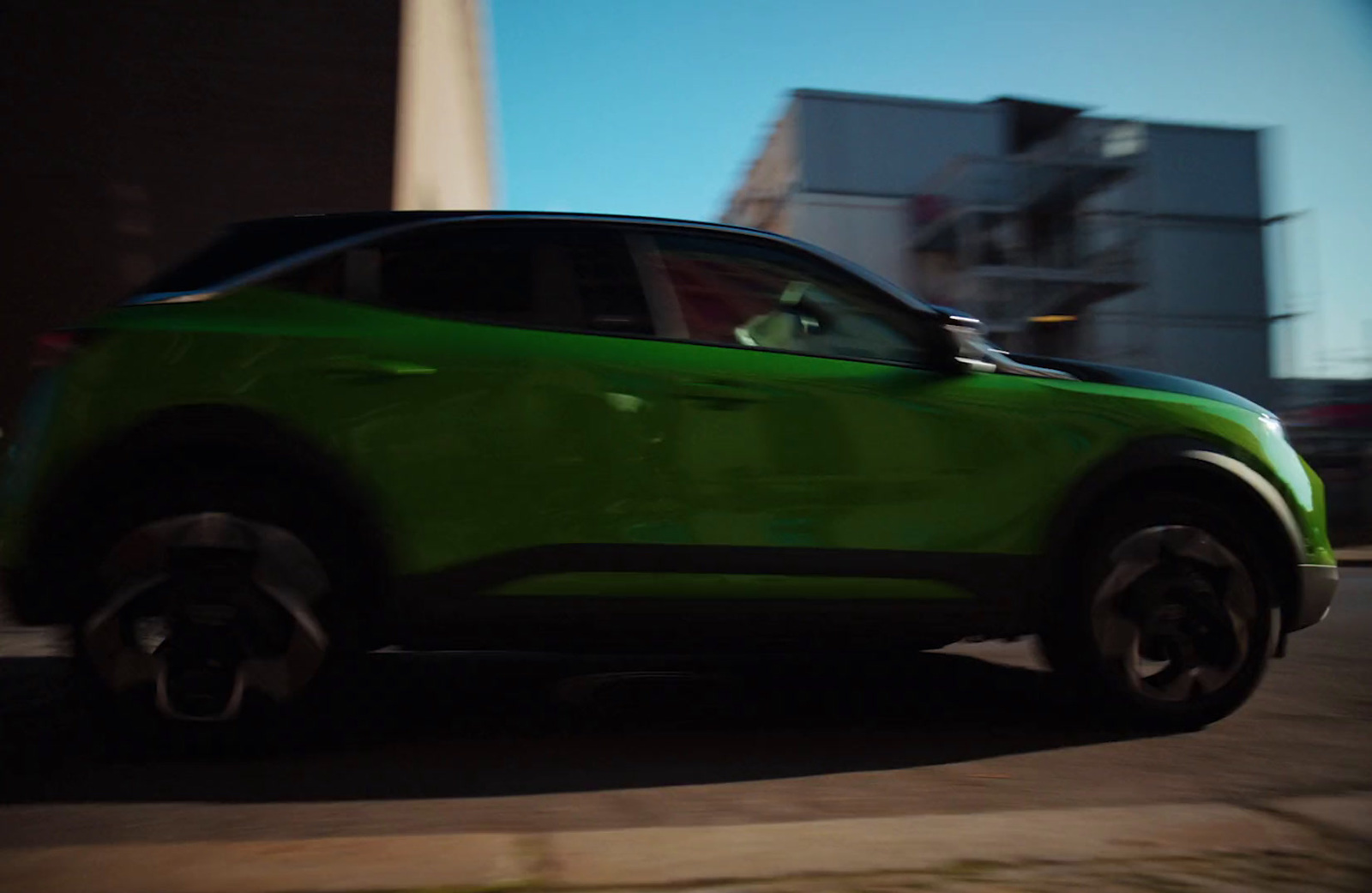 a green car driving down a street next to tall buildings