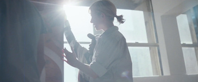 a woman standing in front of a window holding an american flag