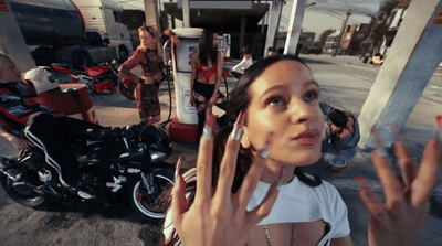 a woman holding up her hand in front of a gas station