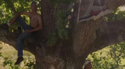 a shirtless man sitting in a tree next to another man