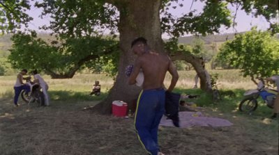 a shirtless man standing in front of a tree