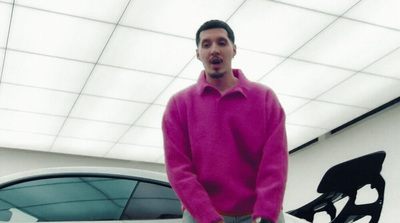 a man in a pink sweater standing next to a white car