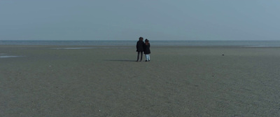 a man and a woman standing on a beach next to the ocean