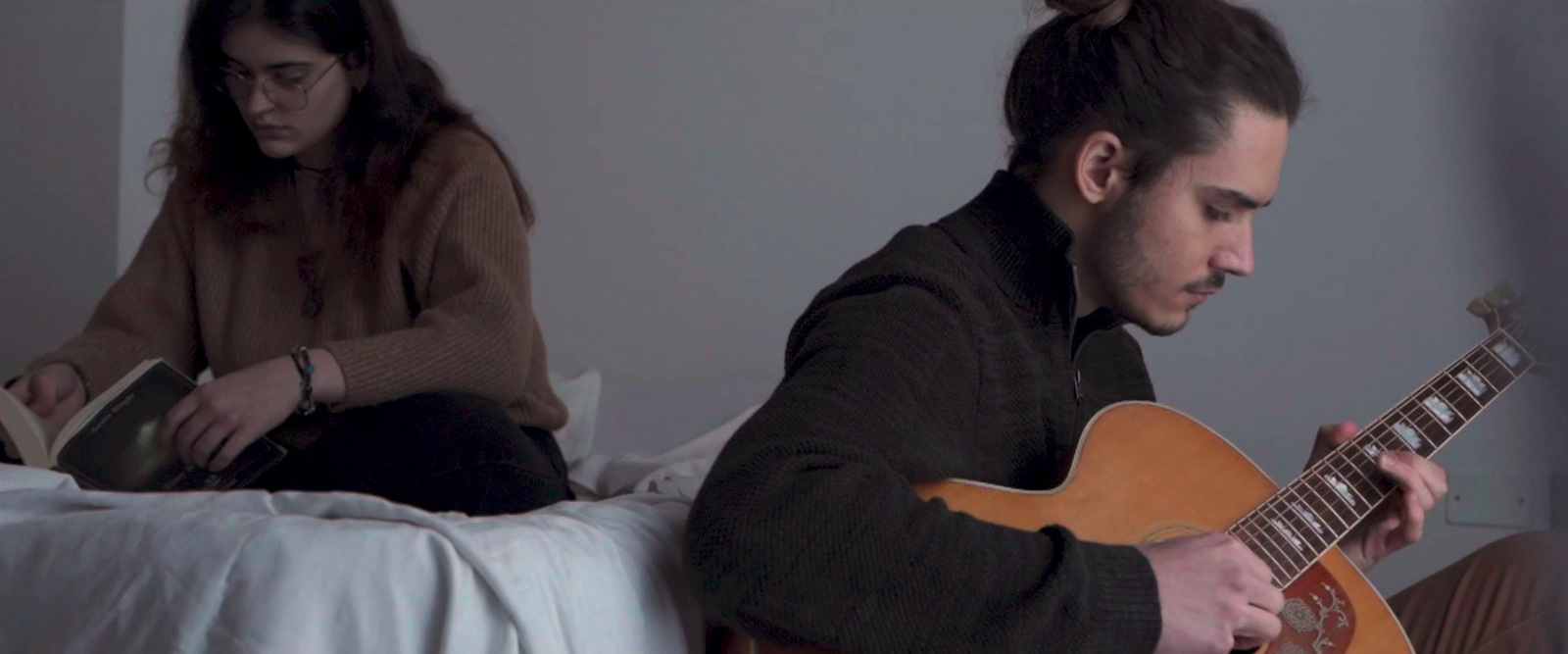 a man sitting on a bed while playing a guitar