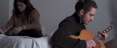 a man sitting on a bed while playing a guitar