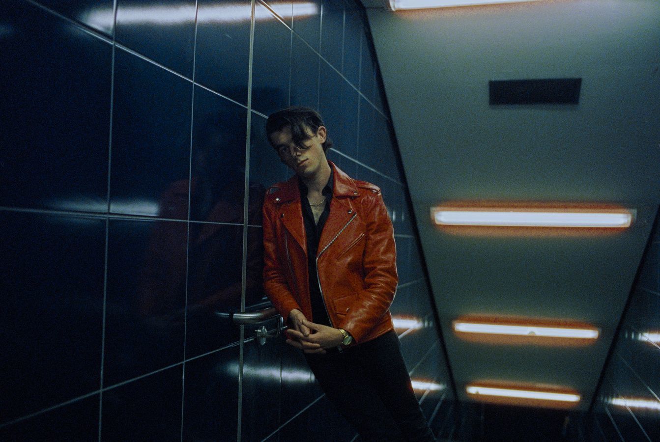 a man in a red jacket leaning against a wall